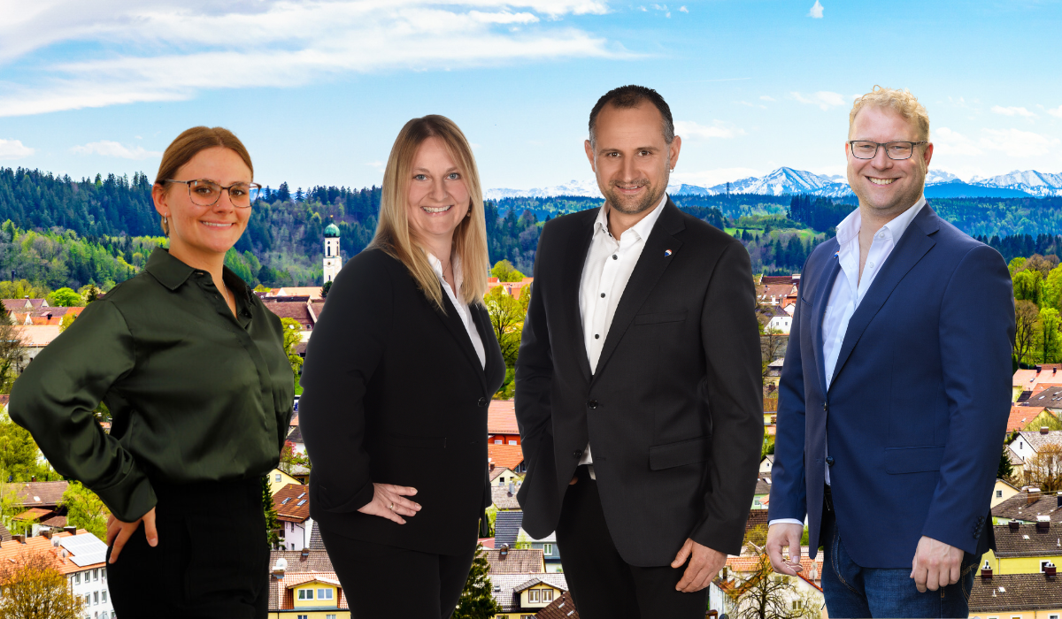 Stockhausen Immobilienteam Schongau - vier Immobilienmakerl vor dem Stadtpanorama Schongau mit Alpenblick und Kirchturm