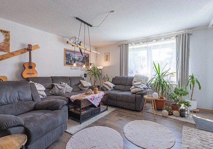 Ger�umiges Wohnzimmer mit Holzboden, gro�er Couch und heellen Fenstern - 3-Zimmer-Wohnung verkauft in Kaufbeuren